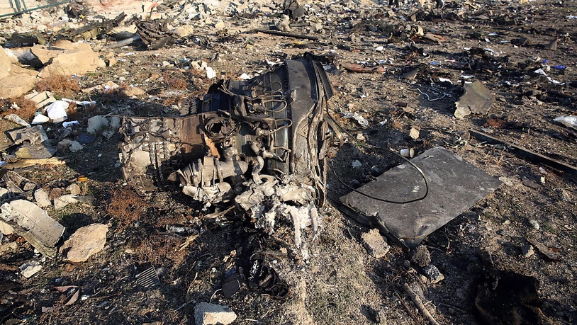 Einer der Flugzeugmotoren der abgestürzten Boeing 737 der Fluggesellschaft UIA liegt zwischen den Trümmern in der Nähe der iranischen Hauptstadt Teheran. Im Hintergrund arbeiten Ermittler an der Aufklärung der Unglücksursache.