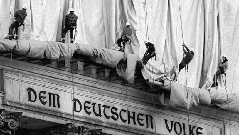 ARCHIV - Gewerbekletterer rollen die Verhüllungsplanen für den Berliner Reichstag vom Giebel des Bauwerks ab. Direkt über dem Haupteingang und der Schrift "Dem Deutschen Volke" fällt bei der Aktion des Verpackungskünstlers Christo der Stoff entlang der…