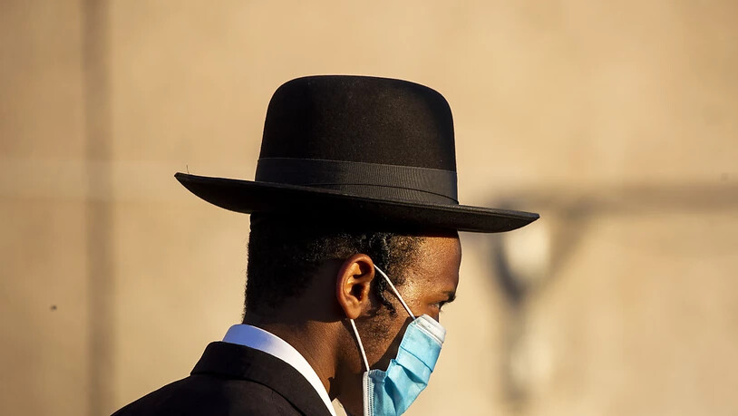 Ein orthodoxer Jude wartet mit medizinischem Mundschutz darauf, eine Straße überqueren zu können. Landesweit sind coronabedingte Beschränkungen in Kraft getreten, nachdem die Zahl der Infizierten gestiegen ist. Foto: Ariel Schalit/AP/dpa