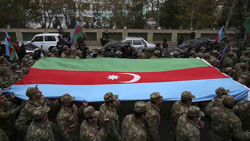 Aserbaidschanische Soldaten tragen eine große Fahne in den Farben ihrer Nationalflagge, während sie die Rückgabe der Region Latschin feiern. Foto: Emrah Gurel/AP/dpa