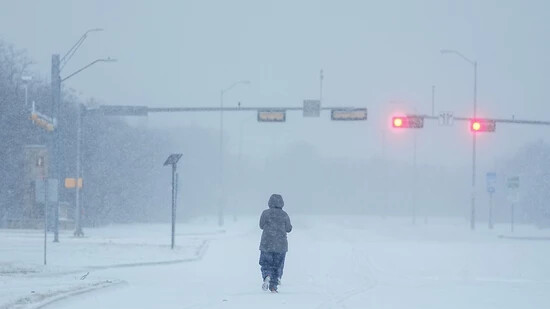Ein Jogger läuft während eines Wintersturms über eine schneebedeckte Straße. Foto: Julio Cortez/AP/dpa