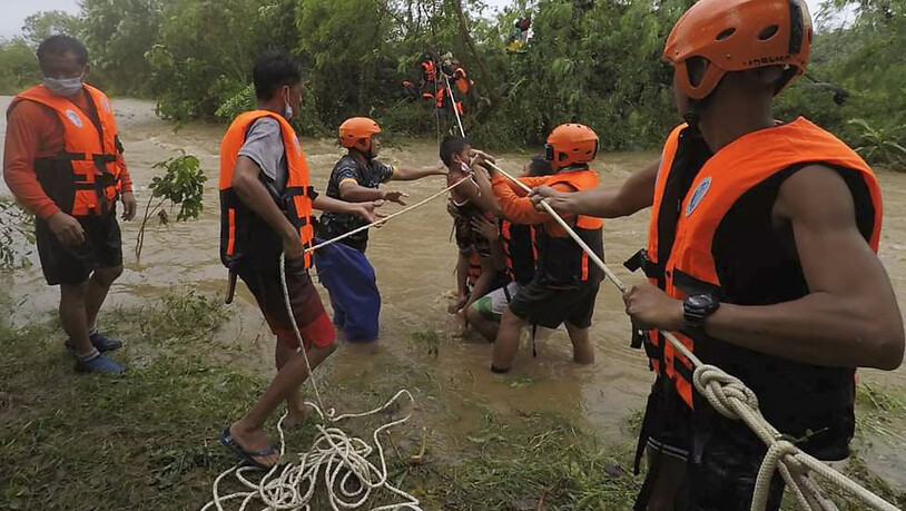HANDOUT - Auf diesem vom Gonzaga Municipal Disaster Risk Reduction and Management Office veröffentlichten Foto helfen Rettungskräfte einem Kind während der Evakuierung durch einen Fluss. Ein schwerer Tropensturm hat auf den Philippinen Erdrutsche und…