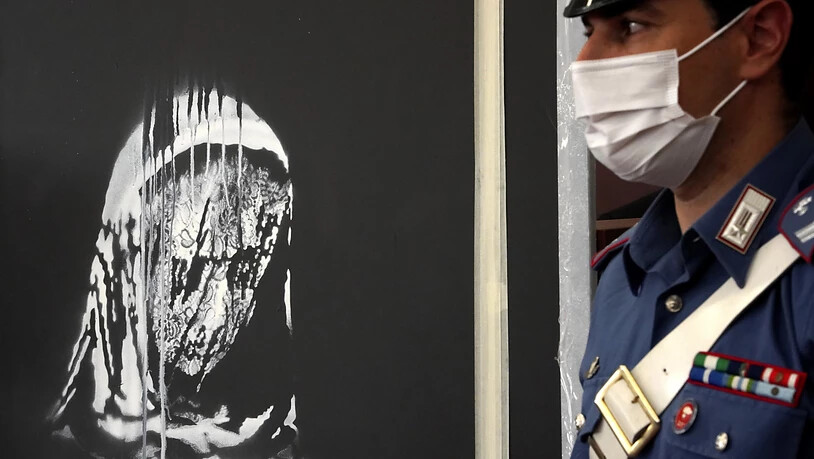 Ein Beamter der Carabinieri steht neben der gestohlenen Tür aus der Pariser Konzerthalle Bataclan, auf der ein dem Streetart-Künstler Banksy zugeschriebenes Graffiti zu sehen ist. Foto: Andrea Rosa/AP/dpa - ACHTUNG: Nur zur redaktionellen Verwendung im…