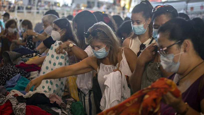 Kundinnen, die Mundschutz tragen, kaufen Kleidung an einem Stand auf einem Markt in Barcelona. Die spanische Region Katalonien führt eine ungewöhnlich strenge Maskenpflicht ein. Foto: Emilio Morenatti/AP/dpa