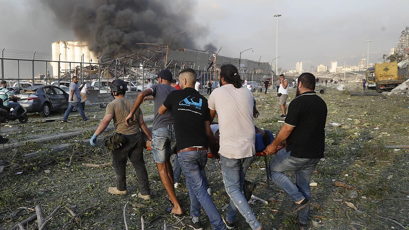 Helfer tragen nach einer schweren Explosion in Beirut ein Opfer, während im Hintergrund Rauch aufsteigt. Foto: Hussein Malla/AP/dpa