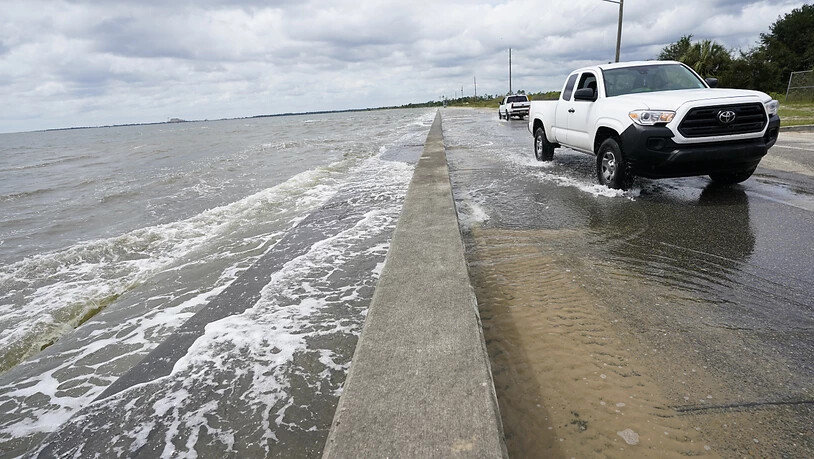 Ein Auto fährt über eine Straße, die durch den Tropensturm mit Meerwasser überflutet ist. Hurrikan «Sally» hat auf seinem Weg in Richtung der US-Golfküste weiter an Kraft gewonnen. Foto: Gerald Herbrt/AP/dpa - ACHTUNG: Nur zur redaktionellen Verwendung…