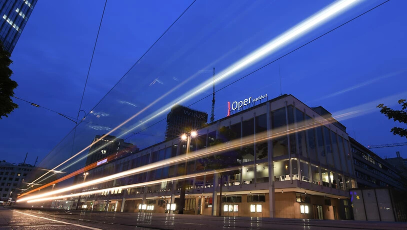 ARCHIV - Lichtspuren einer vorbeifahrenden Straßenbahn sind am Abend am Willy-Brandt-Platz vor den Städtischen Bühnen mit der Oper (r) und dem Schauspiel (l) zu sehen (Langzeitbelichtung). Die Oper Frankfurt und das Grand Theatre de Geneve teilen sich…