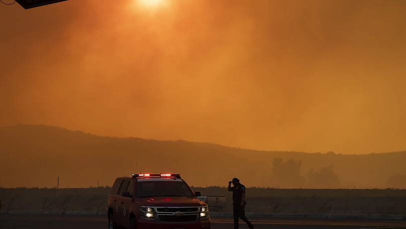 Ein Polizeiauto steht im dichten Rauch eines Waldbrandes. Ein schnell um sich greifendes Feuer hat Einwohner im US-Staat Kalifornien etwa 70 Kilometer südöstlich von Los Angeles aufgeschreckt. Foto: Mindy Schauer/The Orange County Register/AP/dpa
