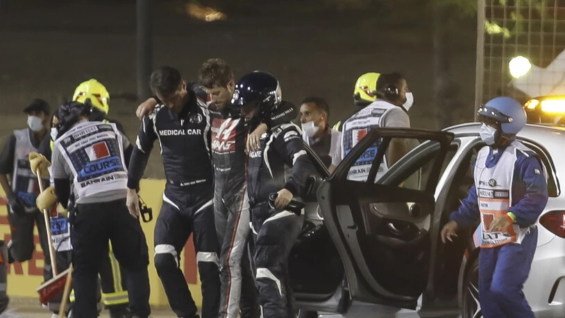 Romain Grosjean (Mitte) wird gestützt zum Auto für die Fahrt in die Klinik an der Strecke gebracht