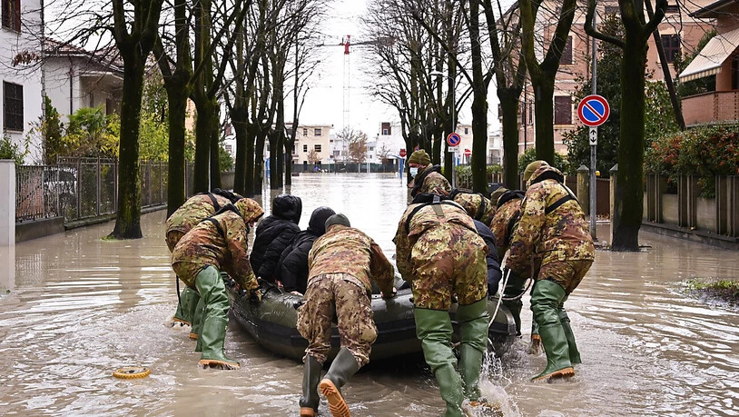Männer schieben ein Boot inmitten einer überschwemmten Straße in einem Wohngebiet an. Die Wetterlage in Italien bleibt nach heftigen Niederschlägen vom Wochenende angespannt, etliche Familien mussten aus ihren Wohnungen evakuiert werden. Foto: Massimo…