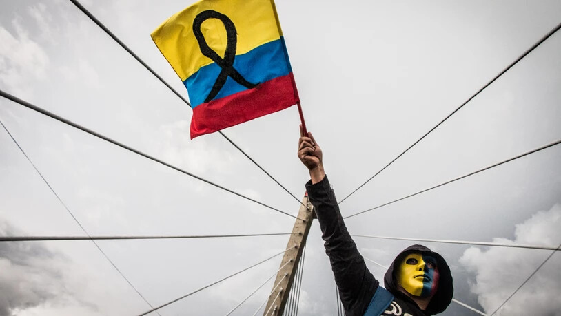 ARCHIV - Ein maskierter Demonstrant schwenkt eine Fahne während einer Kundgebung. Foto: Juan Pablo Otalvaro M/dpa