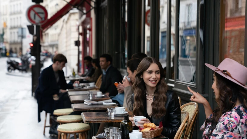 HANDOUT - Emily (Lily Collins, M) sitzt mit einer Freundin im Café - eine Filmszene aus der ersten Staffel der Netflix-Serie «Emily in Paris» (undatierte Aufnahme). In Frankreich spielende TV-Serien wie «Emily in Paris» oder «Lupin» kurbeln den Tourismus…