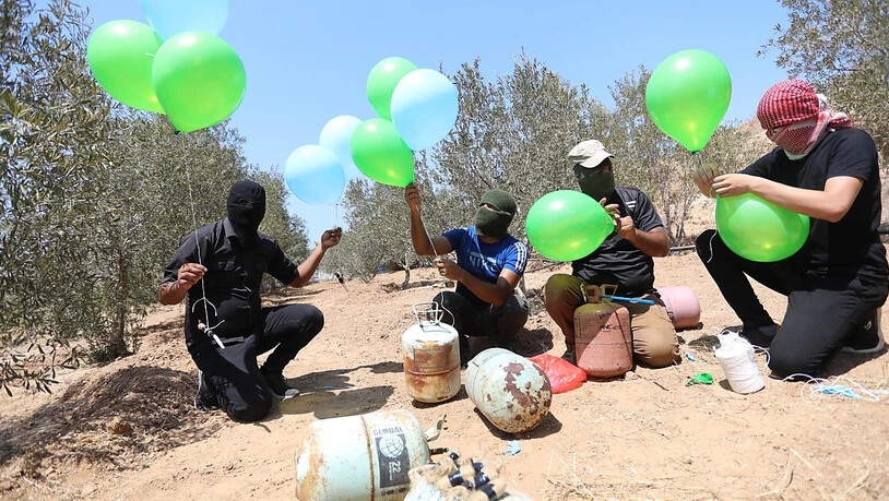 Maskierte Palästinenser bereiten in der Nähe des Lagers Al-Bureij im Zentrum des Gazastreifens Brandballons vor (24.08.2021). Nach Angriffen militanter Palästinenser im Gazastreifen mit Brandballons hat Israels Luftwaffe erneut Ziele in dem…