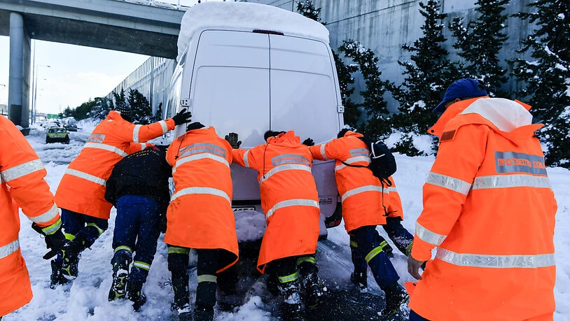 Feuerwehrleute schieben nach einem Schneesturm ein festgefahrenes Fahrzeug von einer Autobahn bei Athen. In Griechenland und der Türkei hat es nach den starken Schneefällen der vergangenen Tage auch am Dienstag weiterhin große Probleme gegeben. Foto:…