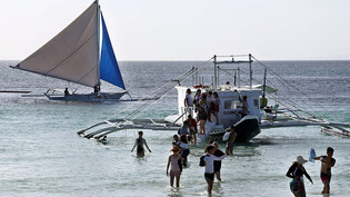 ARCHIV - Eine Gruppe von Touristen steigt am Strand von Boracay aus einem Boot. Die Philippinen öffnen ab kommendem Monat erstmals seit zwei Jahren wieder ihre Grenzen für internationale Touristen. Das kündigte Regierungssprecher Karlo Nograles am…